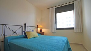 A bedroom with a bed, a nightstand, a lamp, and a window with curtains. - Apartment in Roses near the Beach (Rosas / Roses)