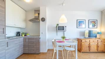 Een moderne keuken met witte kastjes, een eettafel met stoelen, een magnetron en een klok aan de muur.