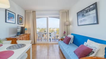 Een moderne woonkamer met een bank, een eettafel en een televisie. Er is een balkon met uitzicht op de stad.