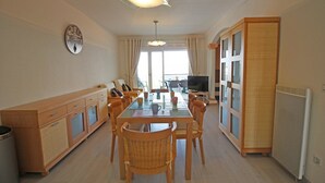 Un comedor con mesa de vidrio, sillas de madera, mostrador tipo buffet y televisor.