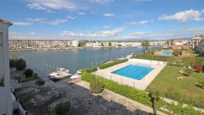 Una piscina con vistas a un río y barcos, rodeada de vegetación y edificios.