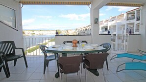 Un balcón con mesa lista para comer, sillas y vistas al mar y edificios.