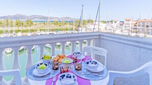 Un balcón con una mesa dispuesta para el desayuno, con vista a un puerto deportivo con barcos y edificios.