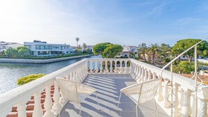 A balcony with white chairs overlooking a canal, with buildings and greenery in the background. - Villa in Empuriabrava with Private Mooring (Empuriabrava)