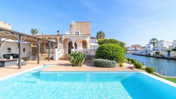 A swimming pool with a view of a stone building and a canal. - Villa in Empuriabrava with Private Mooring (Empuriabrava)