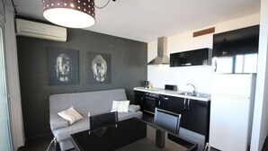 A compact living space with a sofa, a dining table, a kitchen area with a microwave, and a refrigerator.