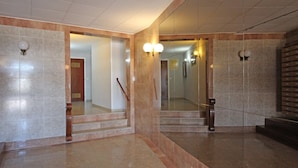 A hallway with marble flooring, a wooden staircase, and a mirrored wall.
