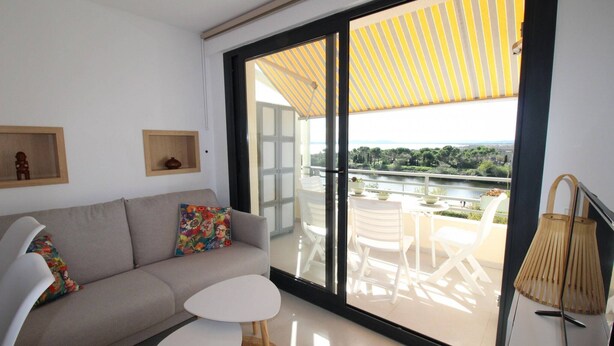 Una sala moderna con un sofá, una mesita y un balcón con mobiliario exterior.