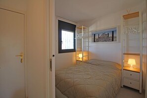 Ein Schlafzimmer mit einem Bett, einem Fenster, einem Nachttisch mit Lampe und einem an der Wand befestigten Regal.