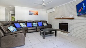 A modern living room with a sectional sofa, a flat-screen TV, a fireplace, and a ceiling fan.