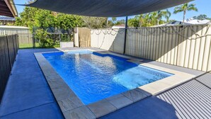 A rectangular swimming pool with a blue interior, surrounded by a concrete deck and a metal fence.