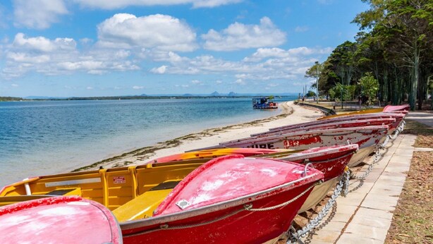 A row of boats lined up on a beach with a clear sky and distant mountains.
