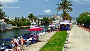 A marina with boats docked, a kiosk, and a clear view of the water and mountains in the background. - Apartment in Empuriabrava with Canal Views (Empuriabrava)