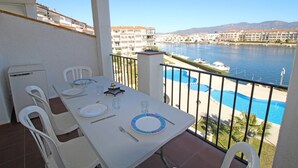 A balcony with a dining table set for two, overlooking a marina and a swimming pool. - Apartment in Empuriabrava with Canal Views (Empuriabrava)