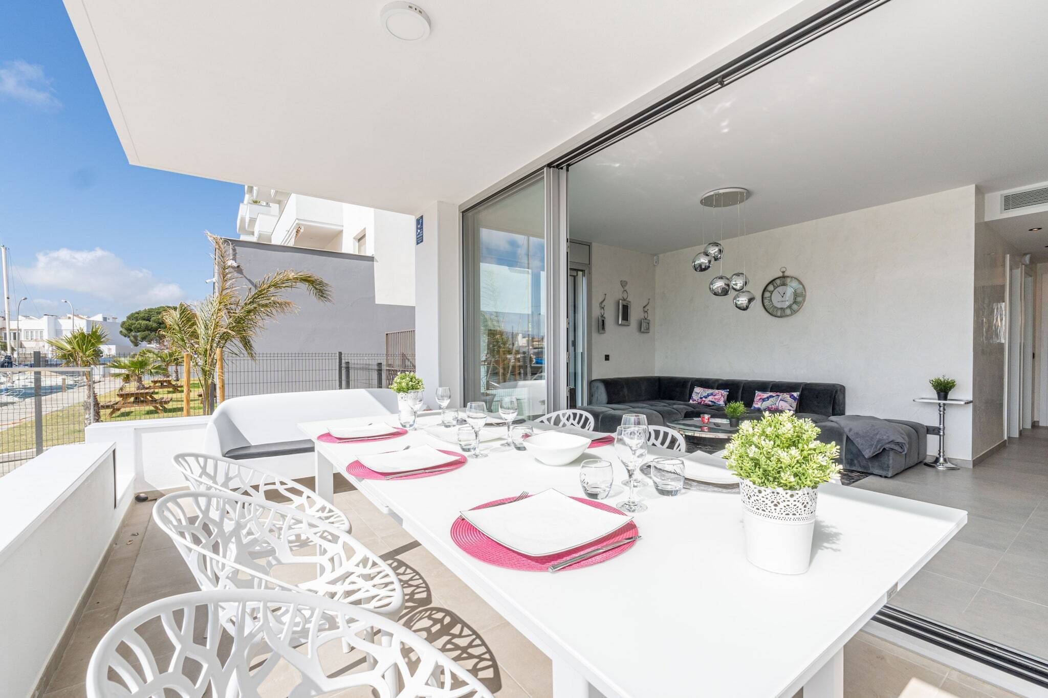 A modern outdoor dining area with white furniture and a glass partition.