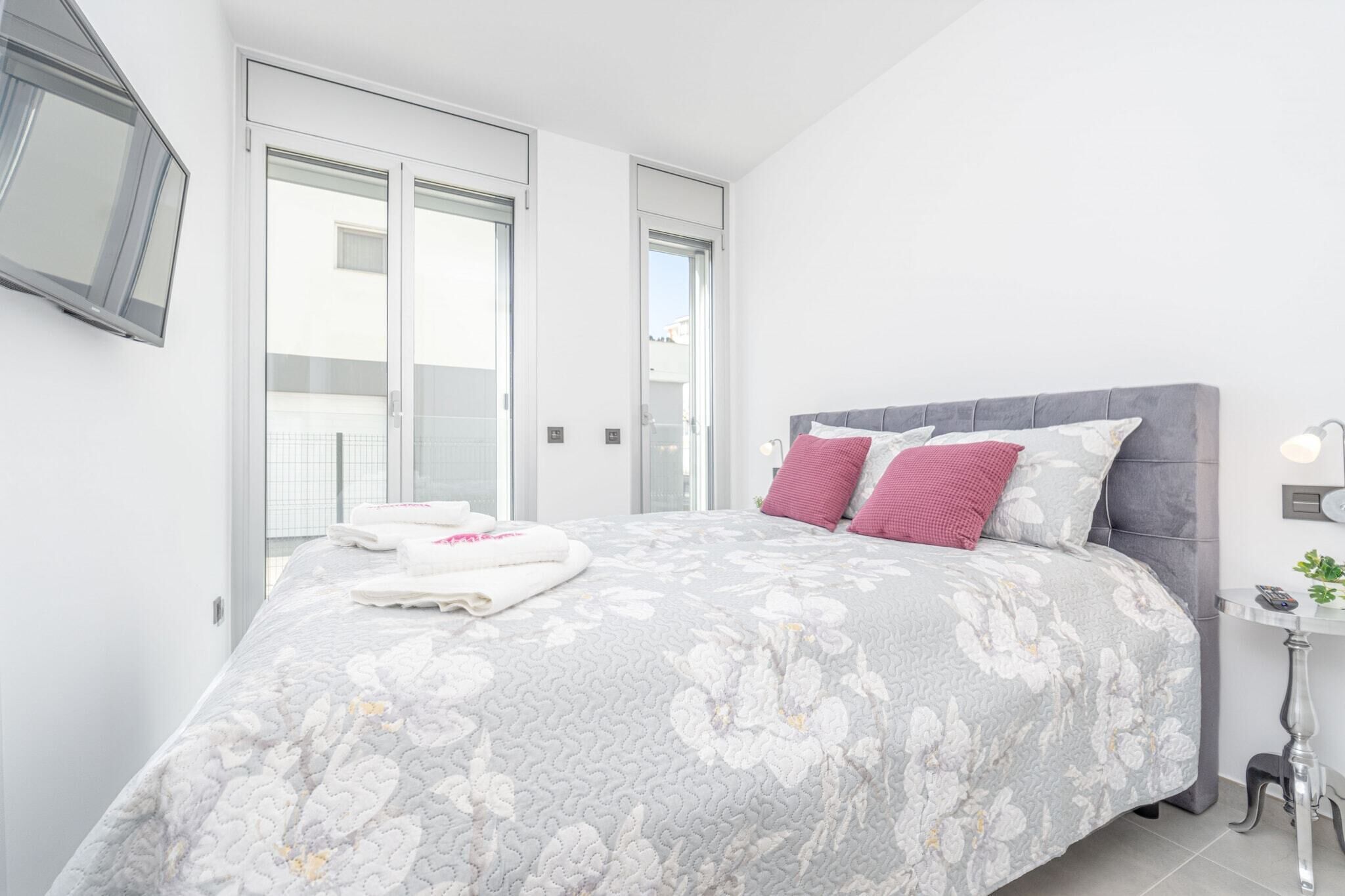 A modern bedroom with a large bed, grey floral bedding, and a grey headboard.