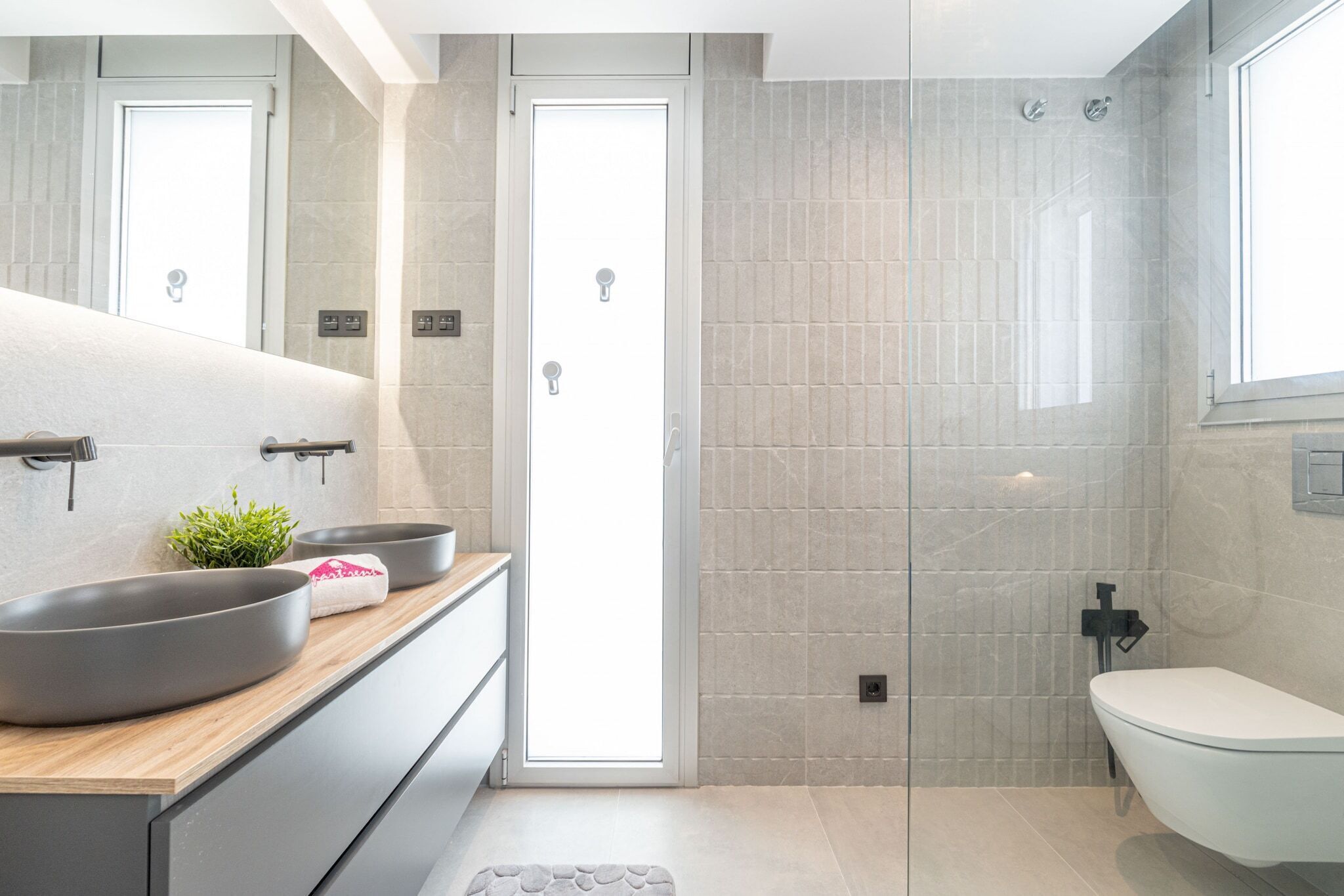 A modern bathroom with a large mirror, two sinks, a shower, and a toilet.