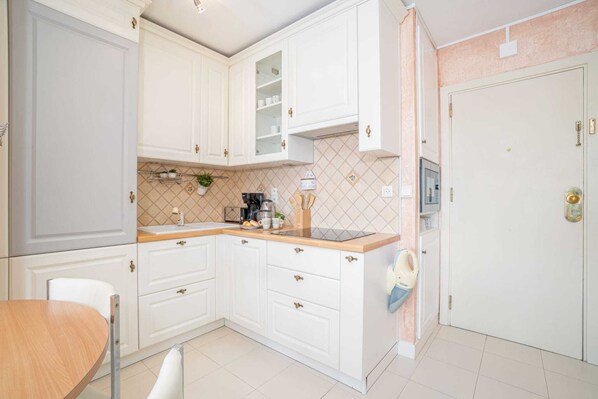 A kitchen with white cabinets, a wooden countertop, and a sink. There is a dining table with chairs and a baby bouncer hanging on the wall.