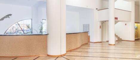 A spacious lobby with a curved reception desk, large pillars, and a staircase leading to an upper level.