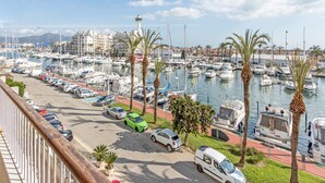 A marina with boats docked, a lighthouse, and a road with parked cars. - Apartment in Empuriabrava with Canal Views (Empuriabrava)