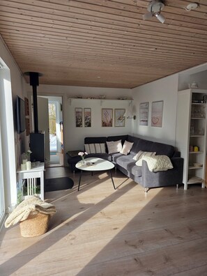 Een moderne woonkamer met een houten plafond, een zwarte bank, een witte salontafel en een boekenkast.
