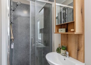 A modern bathroom with a glass-enclosed shower, a white sink, and a wooden medicine cabinet.