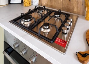 Een keuken met een roestvrijstalen fornuis, vier kookplaten en een inbouwoven.