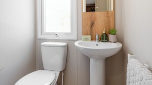 A bathroom with a toilet, a sink, a mirror, and a window. - Three bedroom caravan, ideal for families and angling groups. (Peterborough)