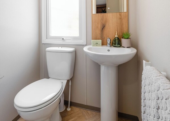 A bathroom with a toilet, a sink, a mirror, and a window. - Three bedroom caravan, ideal for families and angling groups. (Peterborough)