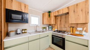 A modern kitchen with wooden cabinets, a black microwave, a stove, and a sink. - Three bedroom caravan, ideal for families and angling groups. (Peterborough)