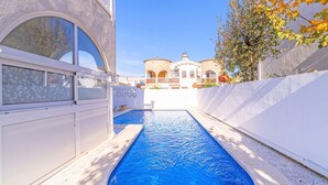 Una piscina con vista a un edificio de ventanas arqueadas y techo de tejas.