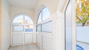 Un pasillo estrecho con baldosas de diseño, una ventana con vistas a un edificio y una puerta con paneles de vidrio esmerilado.
