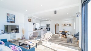 A modern living room with a sofa, coffee table, and chairs, a kitchen area with cabinets and appliances, and a dining area with a table and chairs. - Villa in Empuriabrava with Private Pool (Empuriabrava)