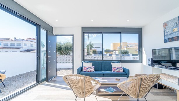 A modern living room with a sofa, two wicker chairs, a coffee table, and a TV. - Villa in Empuriabrava with Private Pool (Empuriabrava)