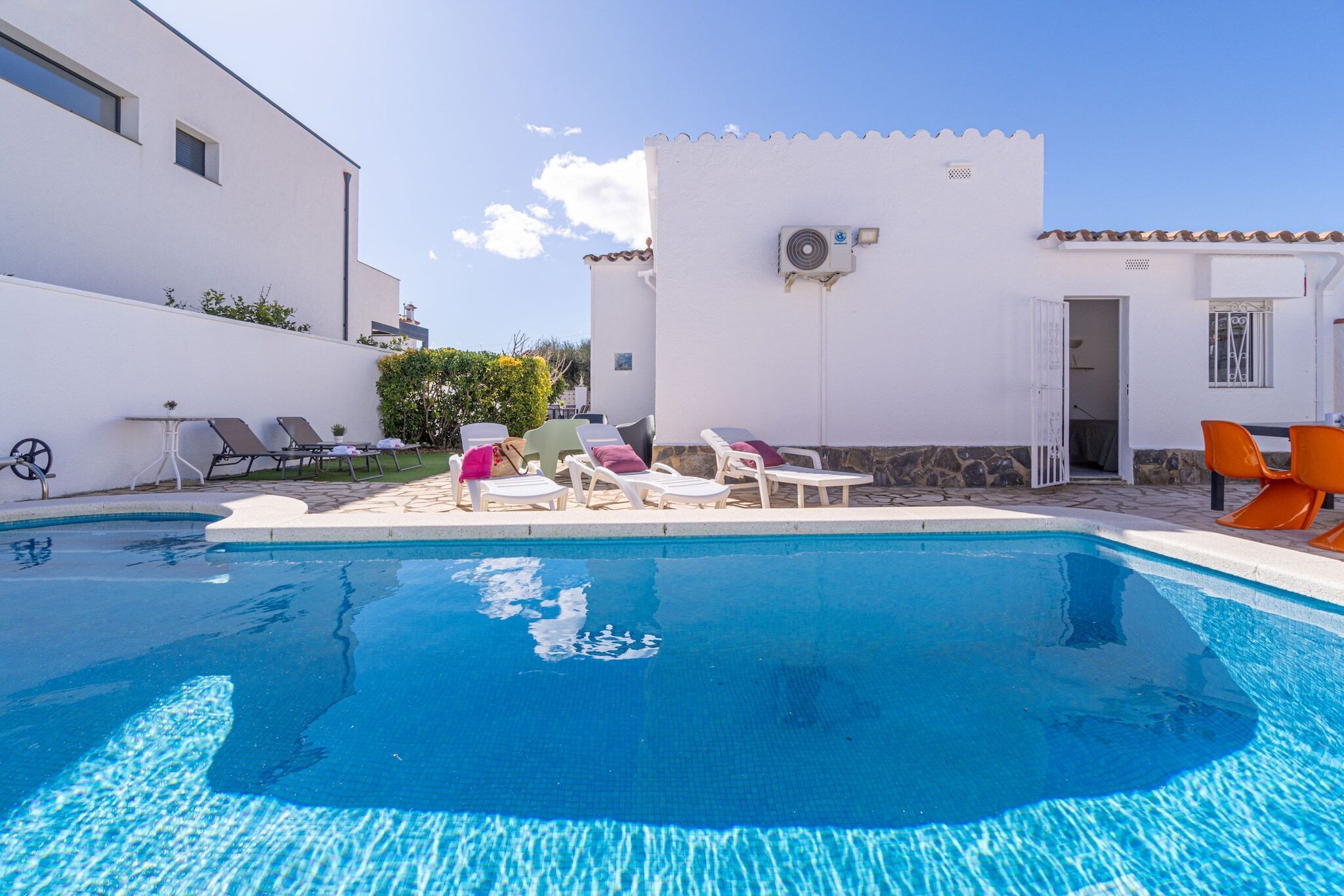 A swimming pool with lounge chairs and a white building with a stone wall.