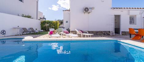 A swimming pool with lounge chairs and a white building with a stone wall.
