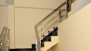 A staircase with a metal handrail and black steps, leading to a landing with a beige wall. - De Classico Residency (Ayodhya)
