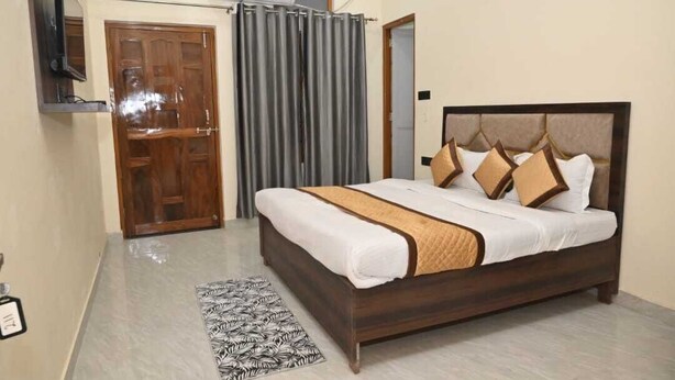 A neatly arranged bedroom with a wooden bed, a television mounted on the wall, and a grey curtain. - De Classico Residency (Ayodhya)