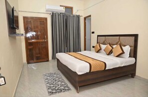 A neatly arranged bedroom with a wooden bed, a television mounted on the wall, and a grey curtain. - De Classico Residency (Ayodhya)