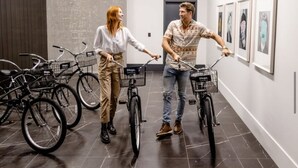 Two people on bicycles in a hallway with bicycles parked against the wall and framed artwork on the wall. - Penthouse High-rise Ocean City Views (San Diego)