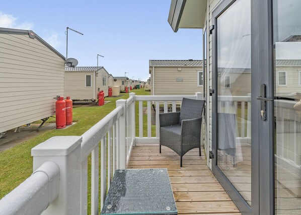 A row of mobile homes with a wooden deck and a glass door leading to a balcony.
