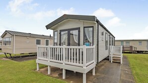 A mobile home with a porch, a small deck, and a window with curtains.