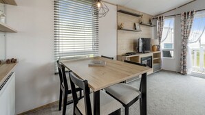 A modern kitchen with a wooden table, chairs, a TV, and a window with blinds.