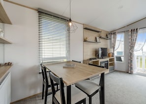 Une cuisine moderne avec une table en bois, des chaises, un téléviseur et une fenêtre équipée de stores.