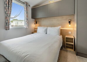Une chambre d’hôtel comprenant un lit, des tables de chevet, une fenêtre avec des rideaux à motifs, une tête de lit dotée d’un éclairage intégré et une vue sur un bâtiment situé à l’extérieur.