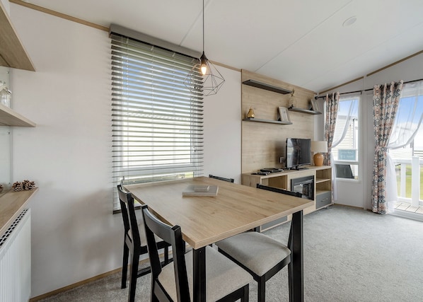 Une cuisine moderne avec une table en bois, des chaises, un téléviseur et une fenêtre équipée de stores.