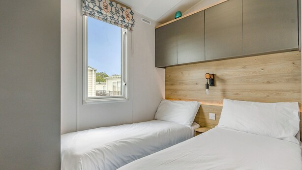 A hotel room with two beds, a window with a view, a wooden headboard, and a small shelf.