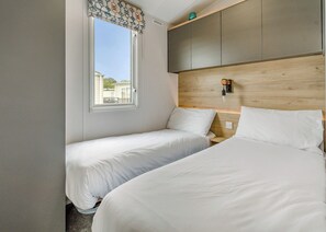 A hotel room with two beds, a window with a view, a wooden headboard, and a small shelf.