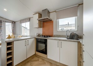 A compact kitchen with white cabinets, a built-in oven, a sink, and a window with a view of a building. - 2 bedroom accommodation in Hornsea (Hornsea)