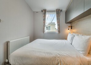 Ein Schlafzimmer mit Bett, Heizkörper, einem Fenster mit Vorhängen und einer Wandleuchte.